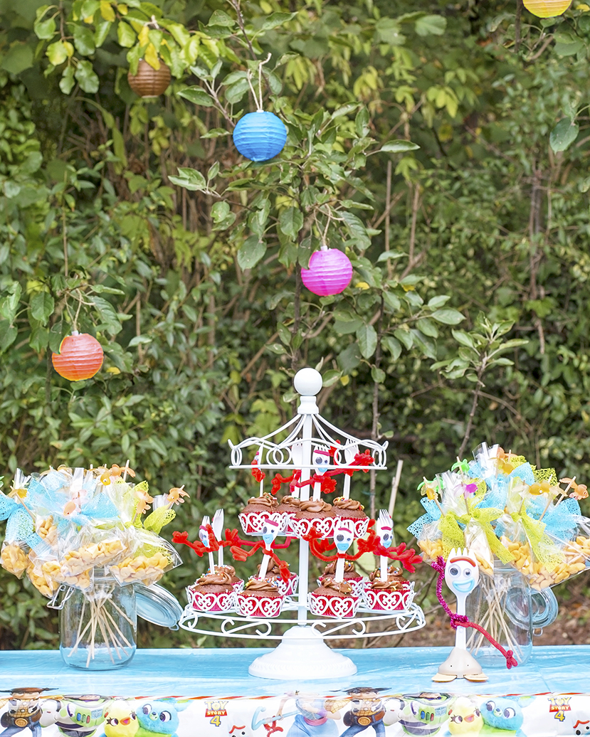 The image shows a party table covered with a food.  There are pepperidge farm fish crackers in little bags on fishing poles with little goldfish on top, and a toy Forky from Disney's Toy Story 4 sits next to a white metal cupcake carousel, filled with Forky cupcakes.