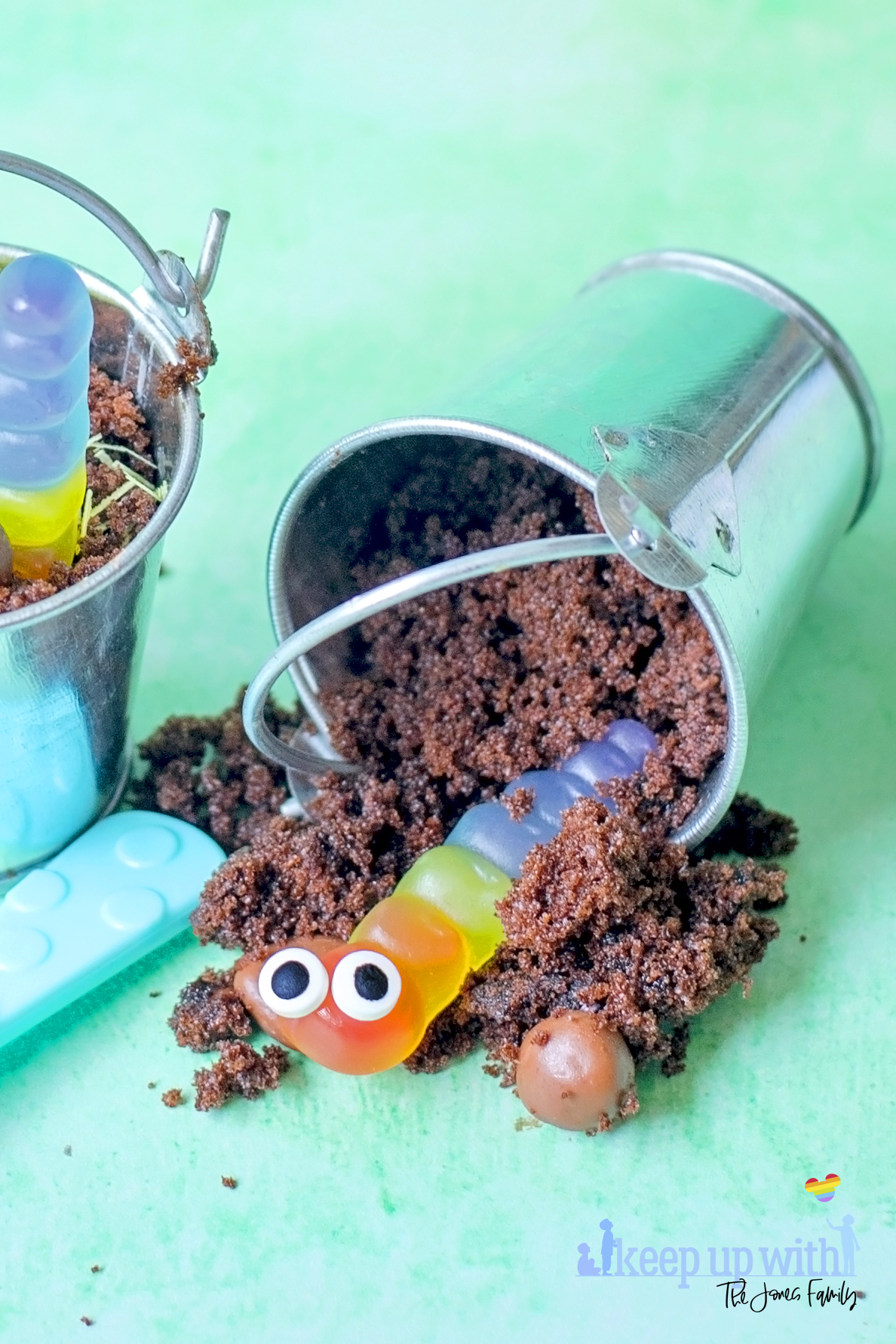 Image shows Buckets of Dirt 'n' Worms Dessert - two little galvanised steel buckets containing chocolate cake made to look like mud and gummy worms with little eyes in them. There are coloured plastic spoons for eating the desserts. Image by Sara-Jayne of Keep Up With The Jones Family.
