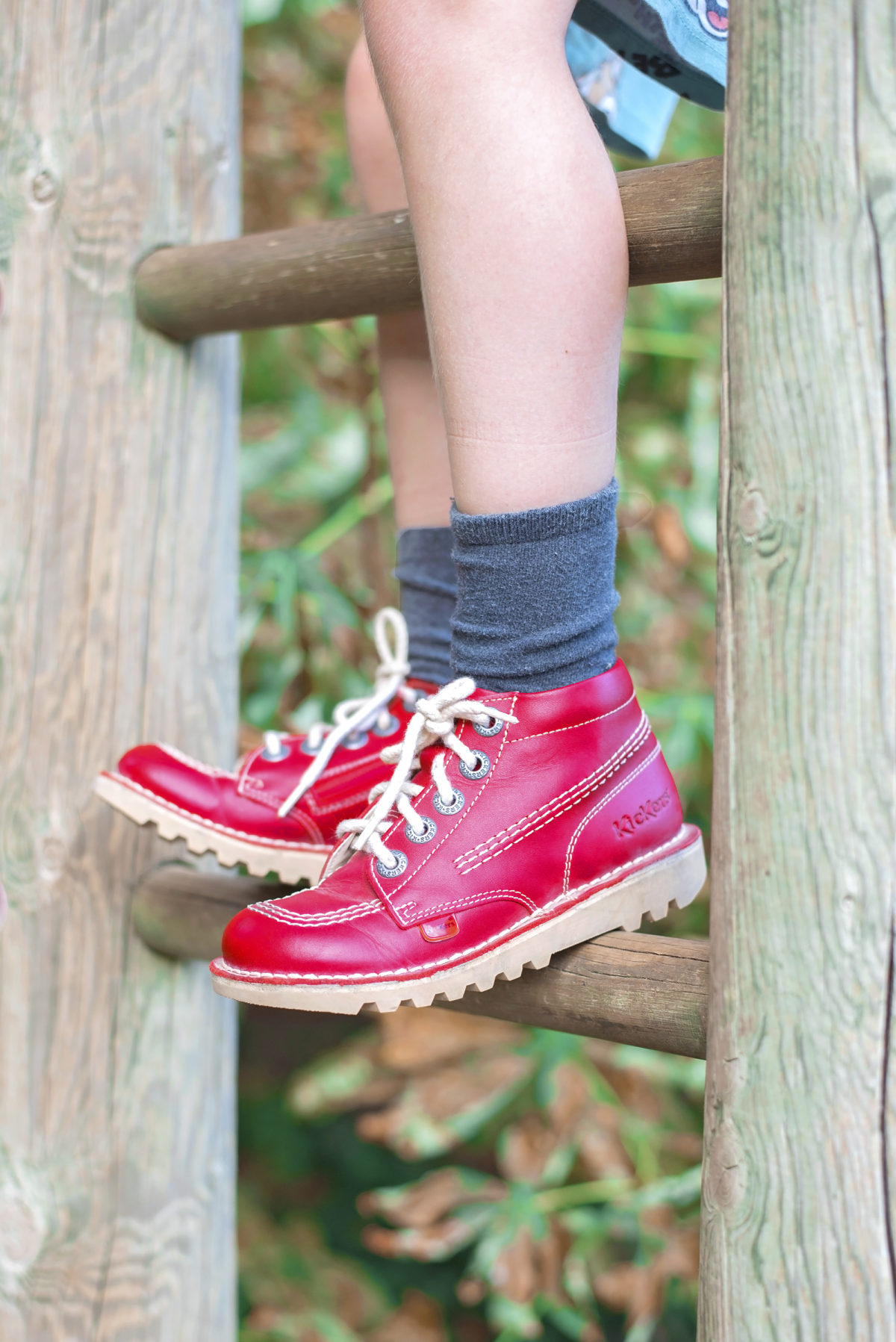 Back to school with Very.co.uk. Red kickers boots resting on a wooden playground ladder being worn by a boy with grey socks.